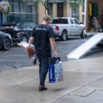 Moving Co. mover carrying a bag and a wrapped chair to the truck ramp