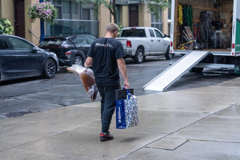 Moving Co. mover carrying a bag and a wrapped chair to the truck ramp