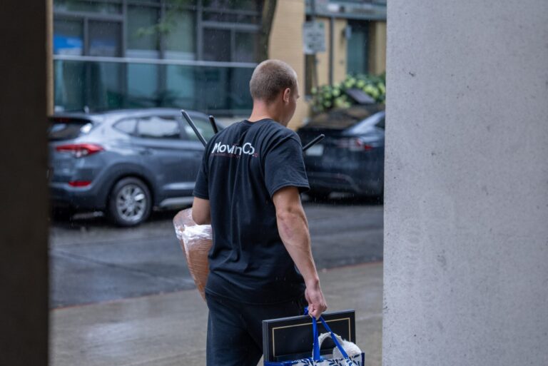 Moving Co. mover carrying bags and a wrapped item out of a building