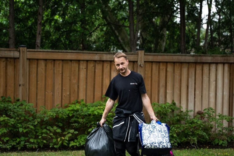 Moving Co. mover carrying full garbage bags across a lawn