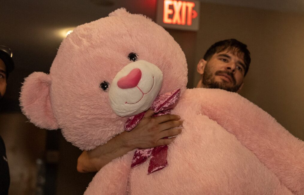 Moving Co. mover carrying a giant pink teddy bear down a hallway