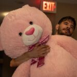 Moving Co. mover carrying a giant pink teddy bear down a hallway