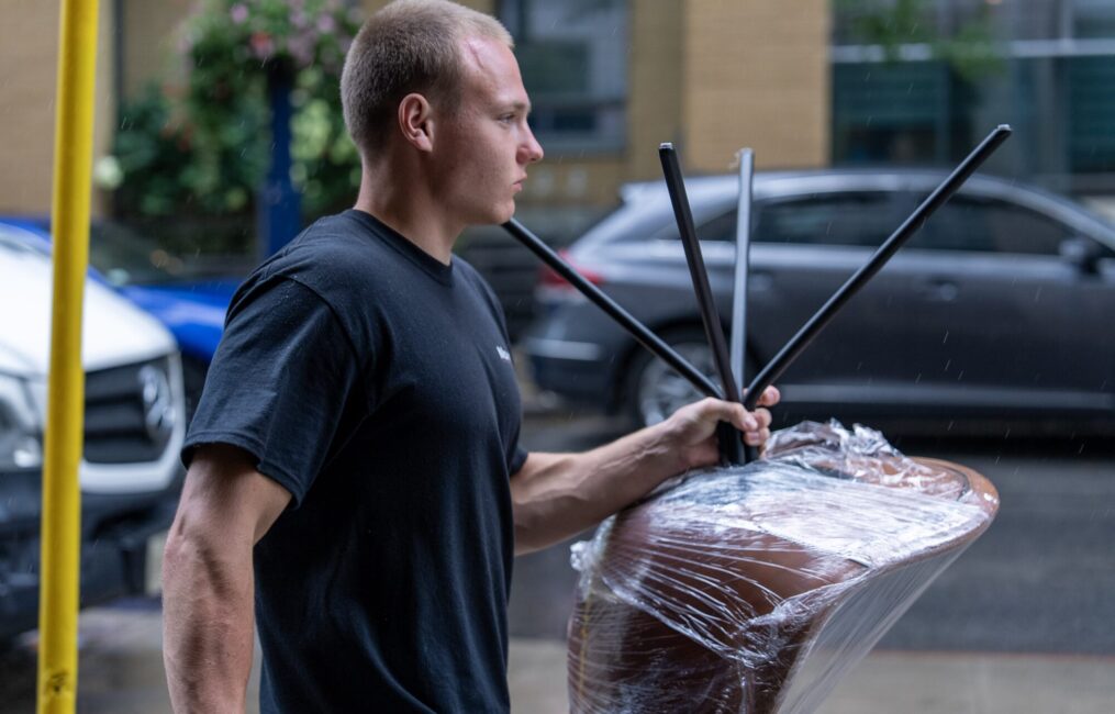 Moving Co. mover carrying a plastic-wrapped chair to the truck