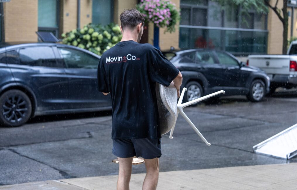Moving Co. mover carrying a wrapped item along a city sidewalk