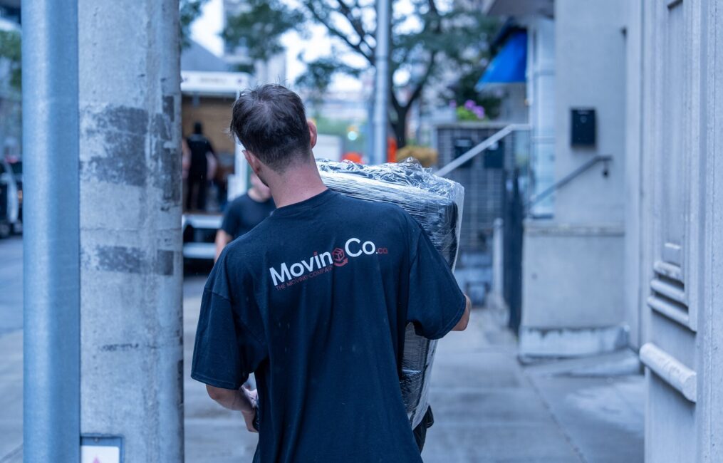 Moving Co. mover with the logo on his shirt carrying a wrapped item down the sidewalk