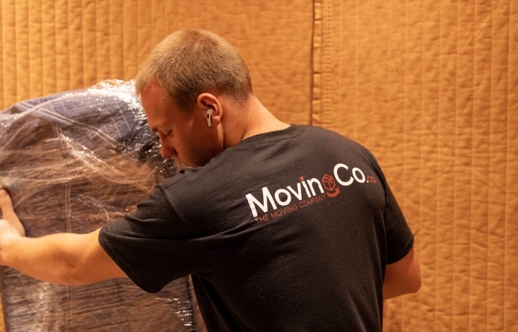 Moving Co. mover with the company logo on his shirt carrying wrapped furniture