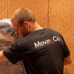 Moving Co. mover with the company logo on his shirt carrying wrapped furniture