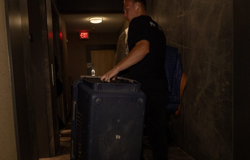 Moving Co. mover rolling a large suitcase down a hallway