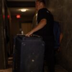 Moving Co. mover rolling a large suitcase down a hallway