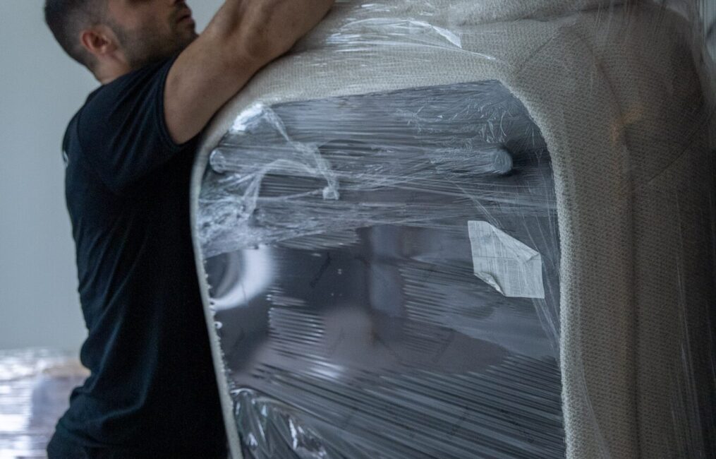 Moving Co. mover shrink-wrapping a tall piece of furniture to protect it for the move