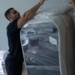 Moving Co. mover shrink-wrapping a tall piece of furniture to protect it for the move