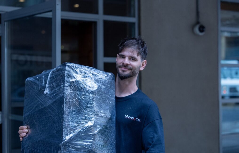 Moving Co. mover smiling while carrying a shrink-wrapped piece of furniture