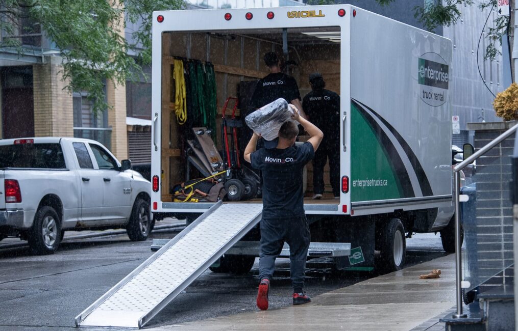 Moving Co. mover carrying a load down the truck ramp on a wet street