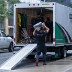 Moving Co. mover carrying a load down the truck ramp on a wet street