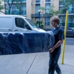 Two Moving Co. movers carrying a blanket-wrapped sofa along the sidewalk