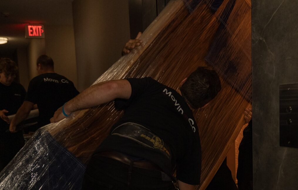 Moving Co. movers carrying a large wrapped item through a doorway