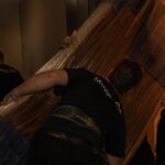 Moving Co. movers carrying a large wrapped item through a doorway