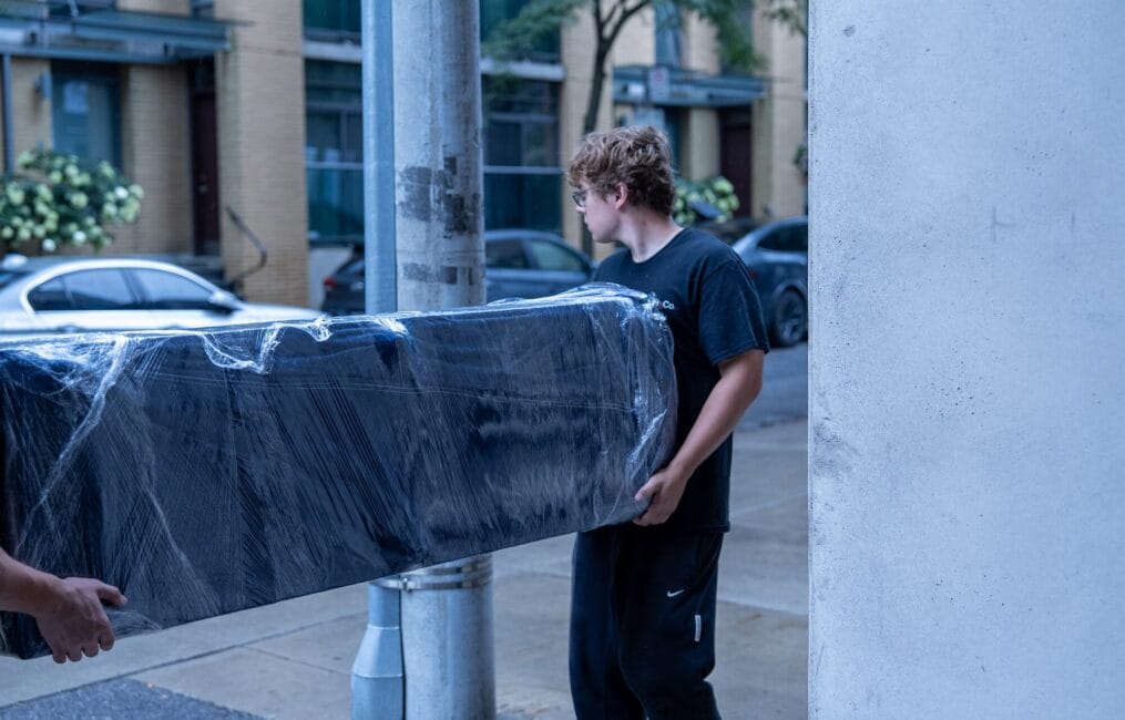 Moving Co. movers carrying a wrapped sofa past a Toronto condo building
