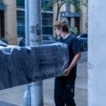 Moving Co. movers carrying a wrapped sofa past a Toronto condo building
