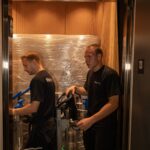 Two Moving Co. movers in a padded condo service elevator with shrink-wrapped furniture