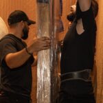 Two Moving Co. movers in a building elevator steadying a tall shrink-wrapped item