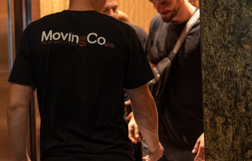 Two Moving Co. movers in a building elevator, the logo on the back of one shirt