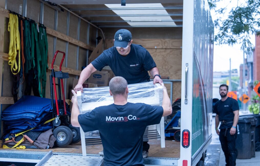 Two Moving Co. movers passing a white shelving unit into the truck