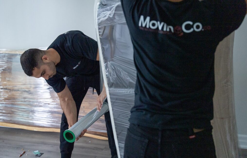 Moving Co. movers shrink-wrapping furniture on the floor of a condo