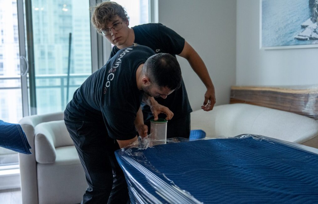 Moving Co. movers wrapping a table in moving blankets and plastic in a condo