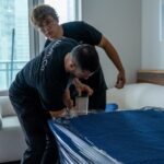 Moving Co. movers wrapping a table in moving blankets and plastic in a condo
