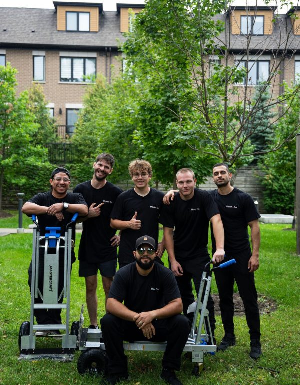The Moving Co. crew posing together with their hand trucks outside a townhouse complex